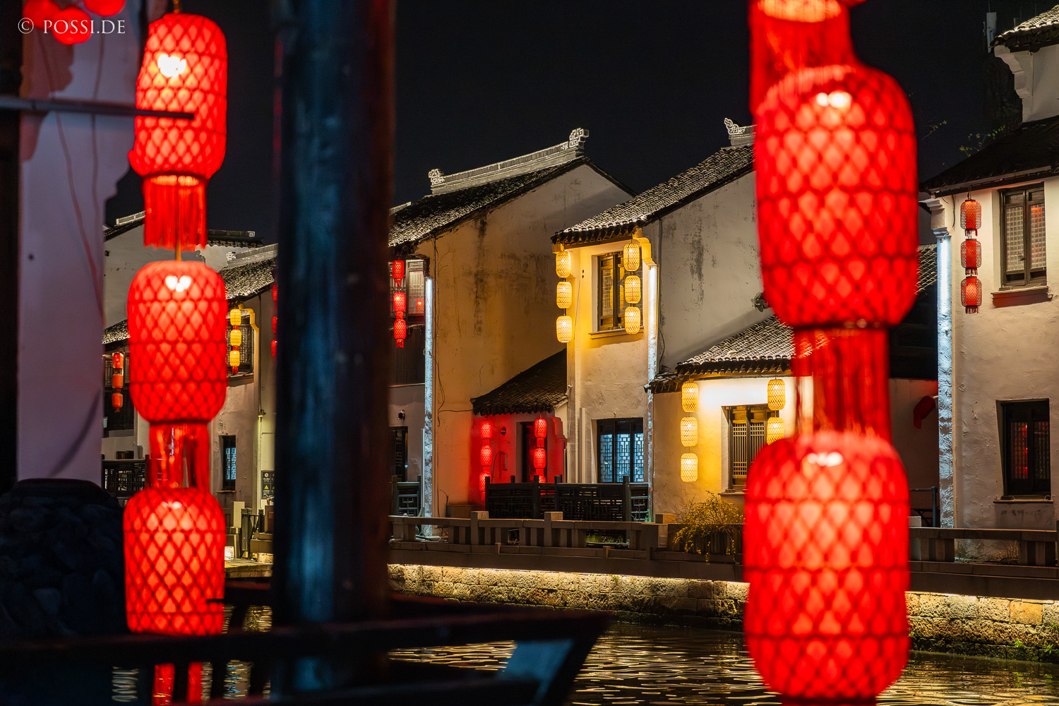 Die Szene zeigt eine idyllische Nachtansicht einer chinesischen Stadt mit traditionellen Gebäuden und roten Laternen. (26.03.2025)