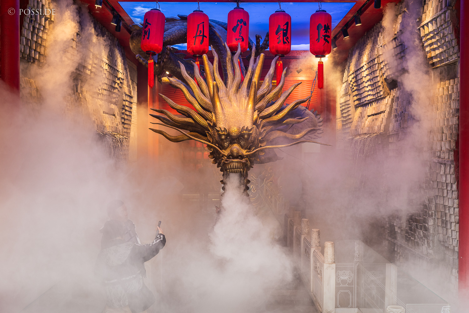 Das Bild zeigt eine Person, die vor einer gigantischen Drachenstatue steht und ein Foto macht. (03.04.2025)