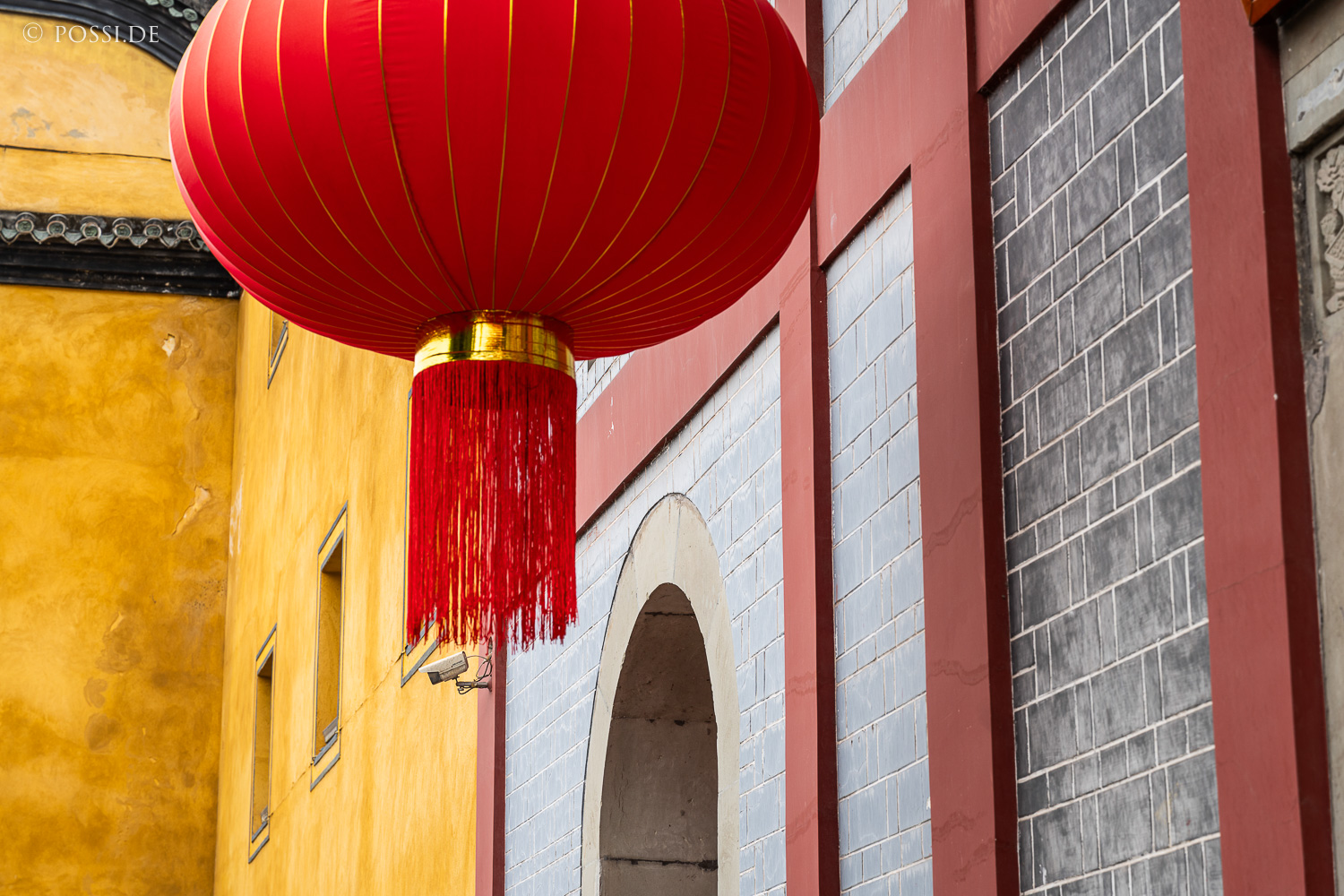 Das Bild zeigt eine rote Laterne vor einer gelben und grauen Wand, die einen asiatischen Stil widerspiegelt. (03.04.2025)